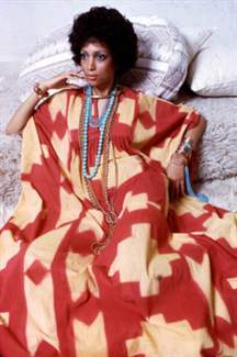 Portrait of an unidentified model, in a red and yellow print dress accented with gold and turquoise jewelry, as she poses on a set of neutral-colored throw pillows, New York, 1970s. (Photo by Anthony Barboza/Getty Images)